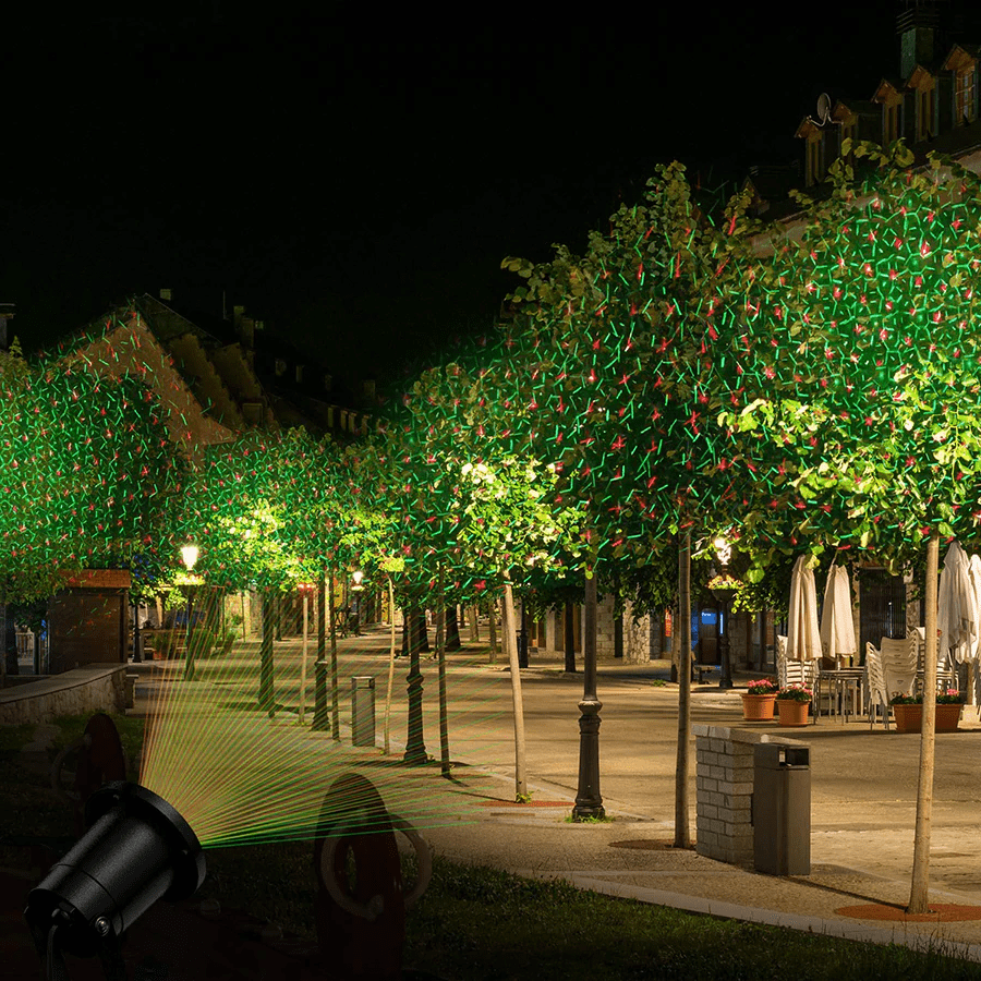 Bright holiday laser light projector casting festive red & green patterns on an outdoor wall or landscape.