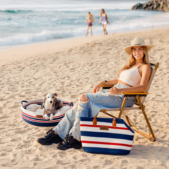 Woman carrying a small dog in a lightweight cotton woven pet carrier beach bag, ideal for summer outings.