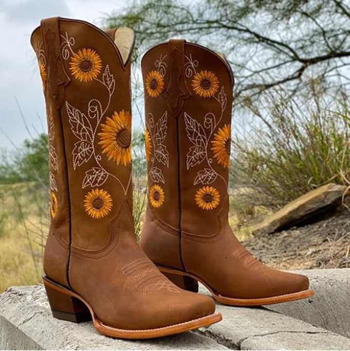 Distressed women's cowboy boots with vibrant sunflower embroidery and a stylish scalloped top. Perfect western statement boots.